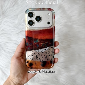 May include: A clear phone case with a colorful abstract design. The case features a mix of red, orange, white, and black patterns. The text "MagSafe Version" is visible at the bottom. The brand name "SookieOfficial" is at the top.
