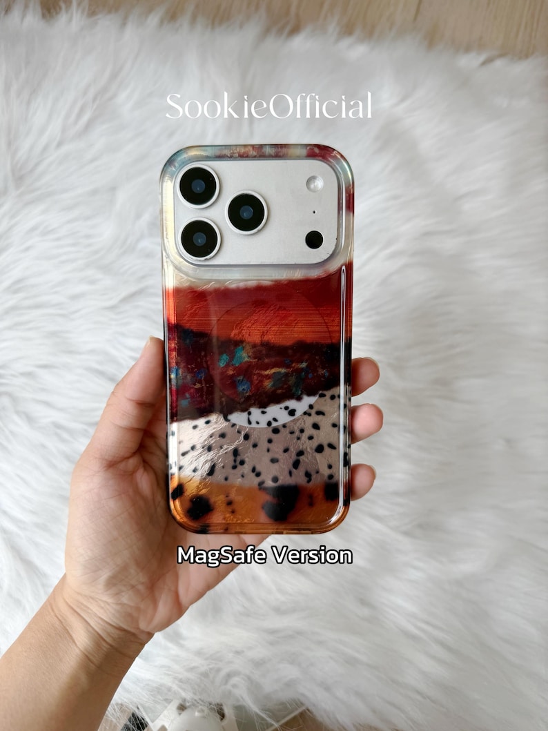 May include: A clear phone case with a colorful abstract design. The case features a mix of red, orange, white, and black patterns. The text "MagSafe Version" is visible at the bottom. The brand name "SookieOfficial" is at the top.
