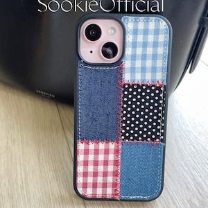 May include: A black phone case with a patchwork design. The case features blue denim, red and white gingham, and black and white polka dots. The case has a stitched design around the edges.