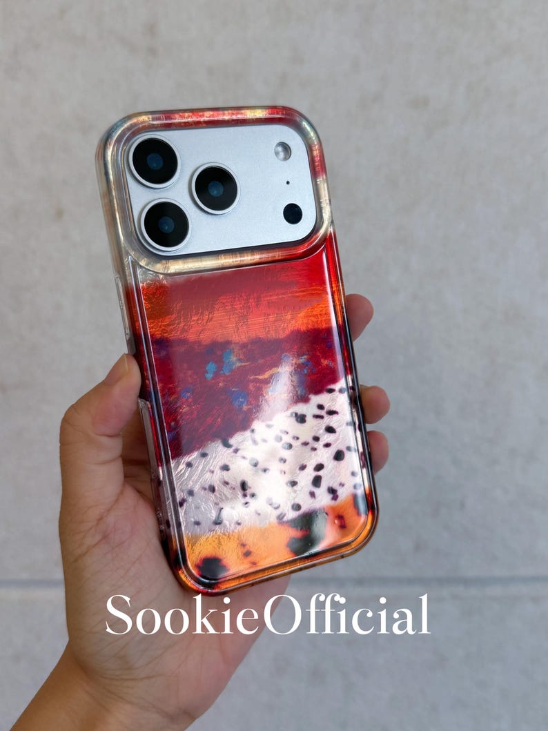May include: A clear phone case with a vibrant abstract design in shades of red, orange, and black. The case has a silver camera module and the text "SookieOfficial" at the bottom. The case is designed to fit a smartphone.