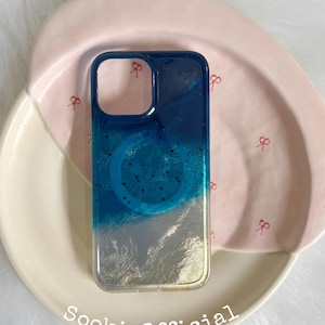 May include: A rectangular phone case featuring a gradient design that transitions from a deep navy blue at the top to a translucent clear base at the bottom. The case includes a circular magnetic ring detail and the text SookieOfficial.