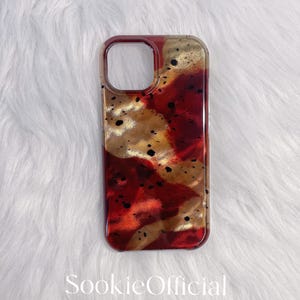 Könnte beinhalten: Transparente Handyhülle mit einem abstrakten Muster in Rot, Gold und Schwarz. Die Hülle hat eine glänzende Oberfläche und eine rechteckige Form mit abgerundeten Ecken. Der Text "SookieOfficial" ist unten aufgedruckt.