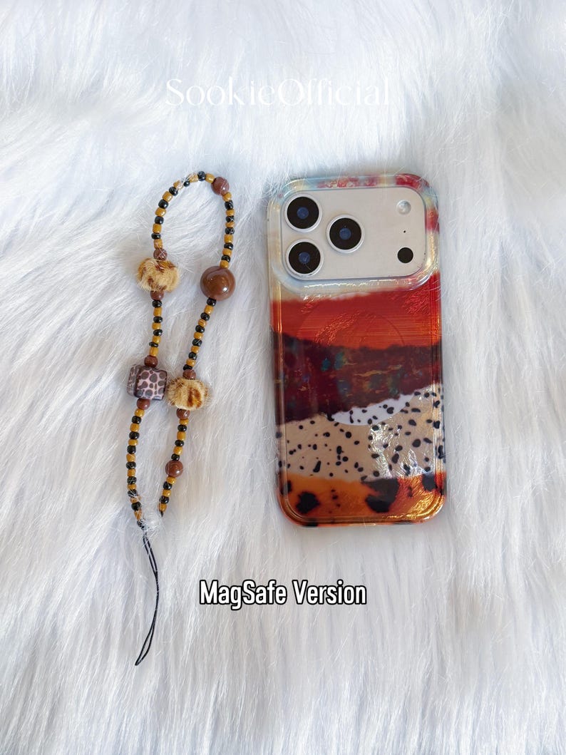 May include: A clear phone case with a colorful abstract design in shades of red, orange, brown, and beige. A beaded phone charm with brown, black, and beige beads is next to the phone case. The text "MagSafe Version" is at the bottom.