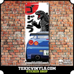 May include: A blue and white banner featuring a cartoon image of a Godzilla-like monster and a blue car with the Japanese text "Godzilla" on the banner. The car has a Japanese number plate with the number 44. The banner also includes the text "Bad Grphx" and "Toxicvinyls.com Sticker Shop".