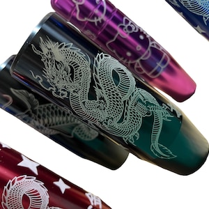 May include: Close-up of several metal gear shift knobs in various colours, including red, black, purple, and blue. Each knob features a unique design, such as a dragon, stars, or a cartoon character. The knobs are angled, showcasing their detailed engravings.