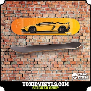 Könnte beinhalten: Ein Skateboard-Deck mit einem gelben Lamborghini-Sportwagendesign auf orangefarbenem Hintergrund. Darunter wird ein leeres Skateboard-Deck gezeigt. Der Hintergrund ist eine Backsteinmauer. Der Text "TOXICVINYLS.COM STICKER SHOP" befindet sich unten.