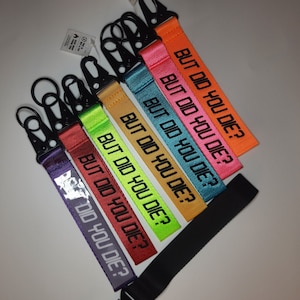 May include: A set of seven colourful keychains with black metal key rings. Each keychain has the phrase "But Did You Die?" printed on it in black.