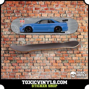 Könnte beinhalten: Ein Skateboard-Deck mit einem Design eines blauen Sportwagens, schwarzen Rädern und einem Heckspoiler. Montiert über einem einfachen Skateboard vor einer Backsteinmauer. Der Text "TOXICVINYLS.COM STICKER SHOP" befindet sich unten.