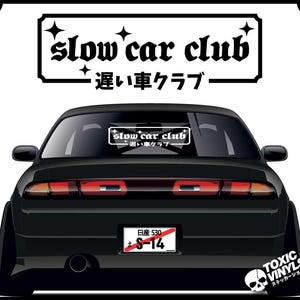 May include: Black car with a white "slow car club" sticker on the rear window. The car has a Japanese number plate that reads "Nissan 530 S-14".