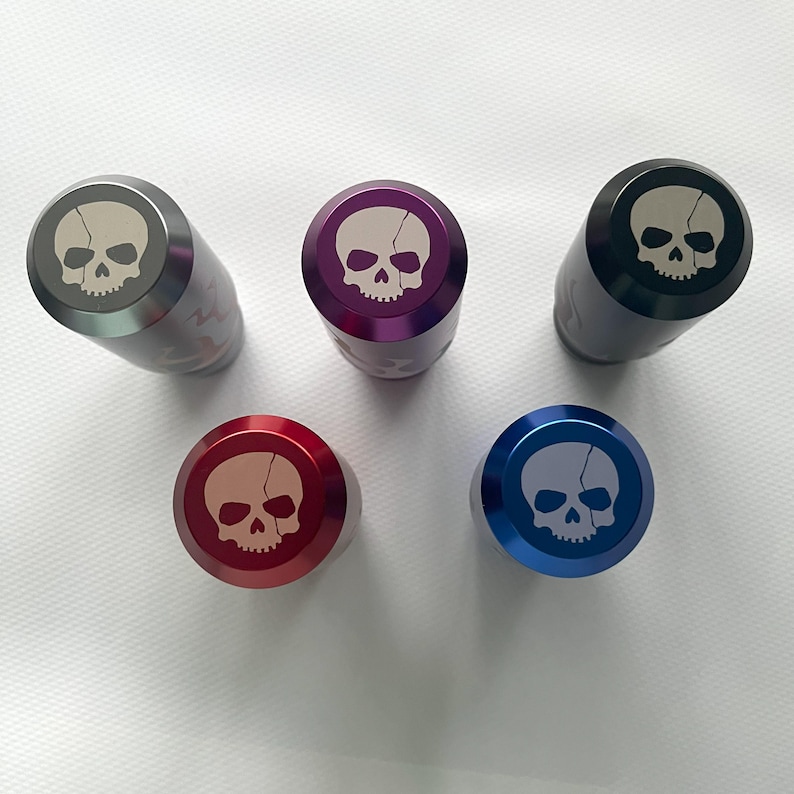 Pu&ograve; includere: Cinque tappi per bottiglia in metallo di diversi colori con un design a forma di teschio. I tappi sono grigi, viola, neri, rossi e blu.