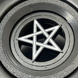 Könnte beinhalten: Ein schwarz-weißes Pentagramm-Design. Der fünfzackige Stern ist in einem kreisförmigen Rahmen zentriert. Der Umriss des Sterns ist weiß und der Hintergrund ist schwarz. Der umgebende Rahmen hat konzentrische Ringe mit einer strukturierten Oberfläche.