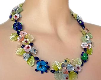 Può includere: Una colorata collana floreale con perline di vetro e dettagli floreali. La collana presenta una varietà di colori, tra cui blu, rosa, verde e giallo. La collana è progettata con forme di foglie e fiori.