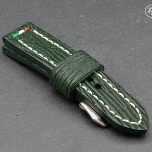May include: A green leather watch strap with white stitching and a green, white, and red accent.