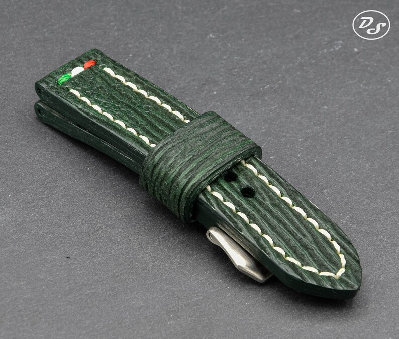 May include: A green leather watch strap with white stitching and a green, white, and red accent.