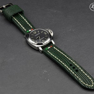 May include: A green leather watch strap with white stitching and a green, white, and red accent. The strap is attached to a silver watch with a black face and white markings.