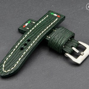 May include: A dark green leather watch strap with white stitching and a silver buckle. The strap has a red, white, and green accent on the top.