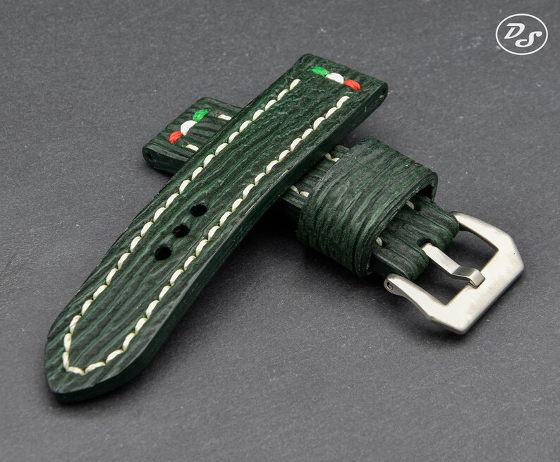 May include: A dark green leather watch strap with white stitching and a silver buckle. The strap has a red, white, and green accent on the top.