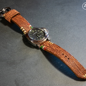 Puede incluir: Una correa de reloj de cuero marr&oacute;n con costuras blancas y verdes. La esfera del reloj es negra con marcas blancas y el texto "LUMINOX" es visible.