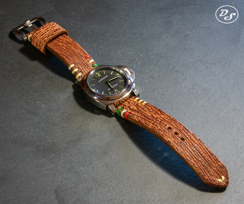 Puede incluir: Una correa de reloj de cuero marr&oacute;n con costuras blancas y verdes. La esfera del reloj es negra con marcas blancas y el texto "LUMINOX" es visible.