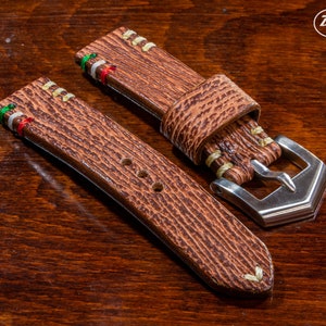 Puede incluir: Dos correas de reloj de cuero marr&oacute;n con costuras blancas y un detalle de rayas de colores. La correa de la derecha tiene una hebilla plateada.