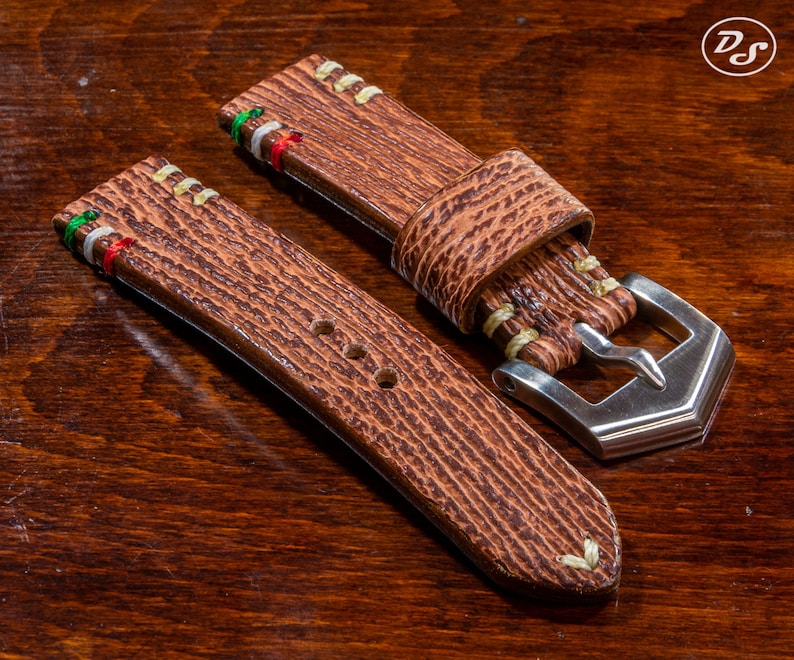 Puede incluir: Dos correas de reloj de cuero marr&oacute;n con costuras blancas y un detalle de rayas de colores. La correa de la derecha tiene una hebilla plateada.