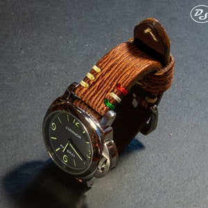 Puede incluir: Una correa de reloj de cuero marr&oacute;n con costuras blancas y detalles coloridos. La correa est&aacute; unida a un reloj plateado con una esfera negra y la palabra "Luminor" impresa en ella.