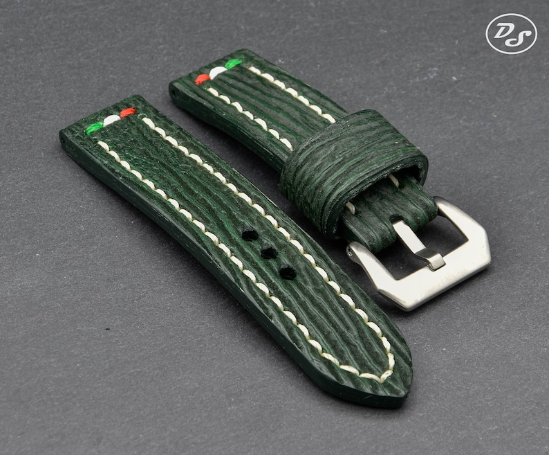 May include: Two green leather watch straps with white stitching and a silver buckle. The straps have a textured surface and a red, white, and green stripe on the top.