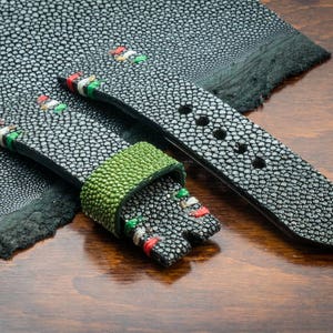 May include: Two black watch straps with a green and white striped pattern. The straps are made of stingray skin and have a textured surface.