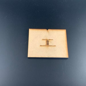 以下が含まれることがあります： 100mm x 80mm の木製ベースで、長方形の切り抜きがあります。ベースは薄い茶色で、「WarchitectsCreations.com」というテキストが印刷されています。