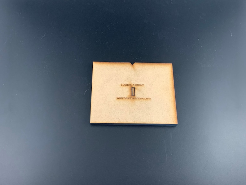 以下が含まれることがあります： 100mm x 80mm の木製ベースで、長方形の切り抜きがあります。ベースは薄い茶色で、「WarchitectsCreations.com」というテキストが印刷されています。