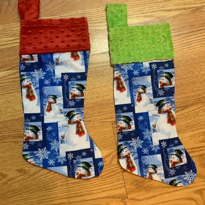 May include: Two Christmas stockings with a snowman pattern. One stocking has a red cuff and the other has a green cuff.