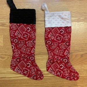 May include: Two red and white Christmas stockings with a bandana print. One stocking has a black cuff and the other has a white cuff.