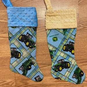 May include: Two Christmas stockings with a blue and yellow plaid pattern featuring John Deere tractors and combines. The stockings have a blue and yellow fleece cuff.