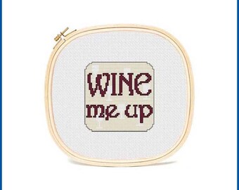 May include: A white cross-stitch embroidery hoop with the phrase "Wine me up" in burgundy lettering.