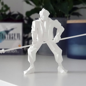 May include: White origami paper model of a character holding a spear. The character is wearing a jacket and pants. The model is standing on a white surface. The background includes a video game case for Final Fantasy VII.