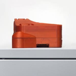 May include: An orange 3D printed object with a rectangular shape and a slot on the bottom.