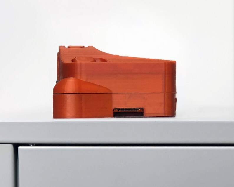 May include: An orange 3D printed object with a rectangular shape and a slot on the bottom.