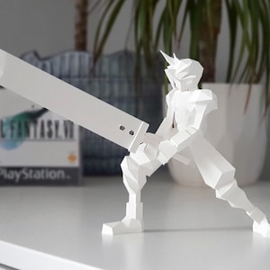 May include: White papercraft model of a video game character holding a sword. The character is in a fighting pose. The model is on a white surface. The video game box for Final Fantasy VII is visible in the background.