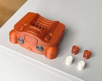 Op de afbeelding: Een oranje Nintendo 64-controller geprint in 3D met vier grijze knoppen en een zwart cartridge-slot. De controller ligt op een wit oppervlak met vier kleine oranje en witte knoppen.