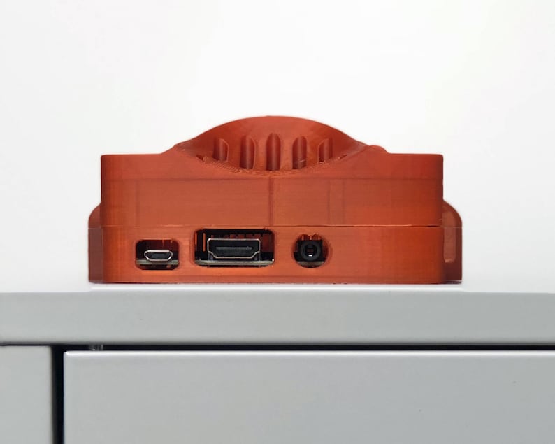 May include: An orange 3D printed case for a Raspberry Pi computer. The case has a raised section on the top and includes ports for HDMI, USB, and power.