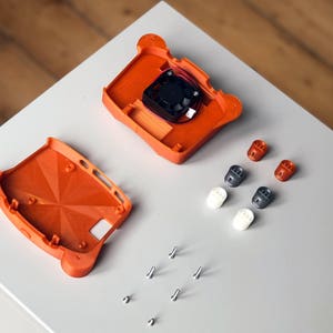 May include: Two orange 3D printed plastic pieces for a case, a small black fan, six small plastic standoffs, and six silver screws.