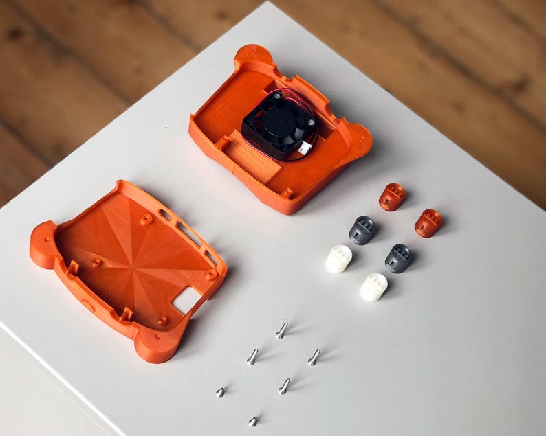 May include: Two orange 3D printed plastic pieces for a case, a small black fan, six small plastic standoffs, and six silver screws.
