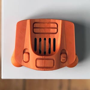 May include: An orange 3D printed model of a Nintendo 64 console.