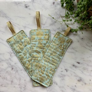 May include: Three light blue fabric bookmarks with gold floral patterns and gold ribbon ties.