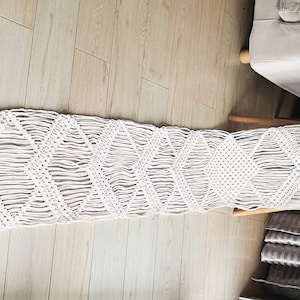 May include: White macrame wall hanging with a diamond pattern. The hanging is made of cotton cord and is approximately 6 feet long.