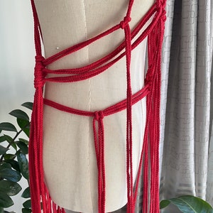 May include: A red crocheted top with long fringe. The top is made of thick rope and has a criss-cross design.