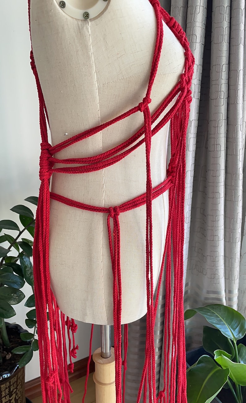 May include: A red crocheted top with long fringe. The top is made of thick rope and has a criss-cross design.