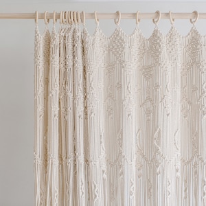 May include: A white macrame curtain with a geometric pattern hangs from a wooden rod.