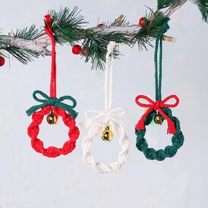 May include: Three handmade Christmas ornaments in the shape of wreaths. The wreaths are made of red, white, and green rope and each has a small gold bell hanging from it.