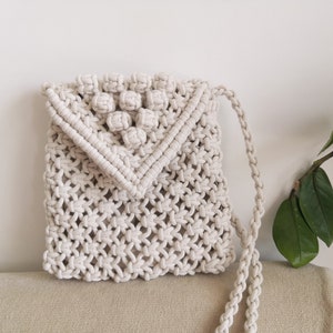 May include: A white crocheted crossbody bag with a knotted design and a flap closure. The bag has a small, decorative tassel on the flap.